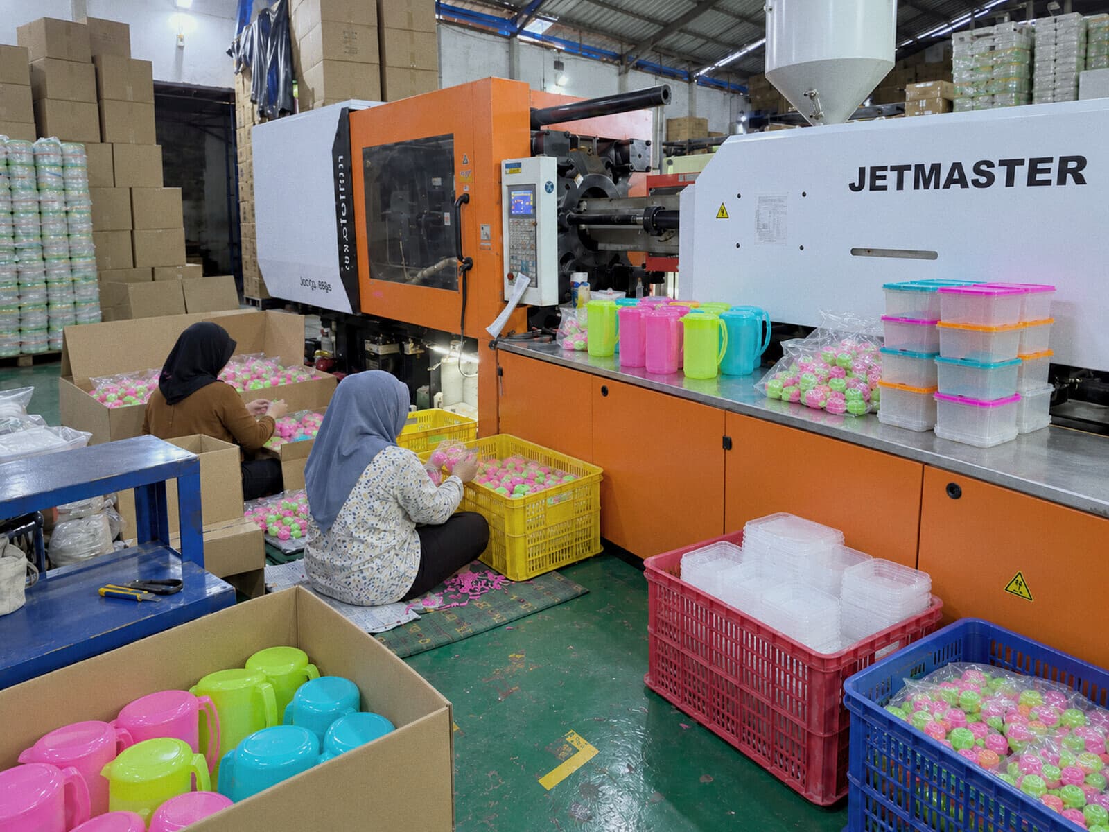 Produk Candid di samping mesin produksi, dengan gudang barang jadi di belakang